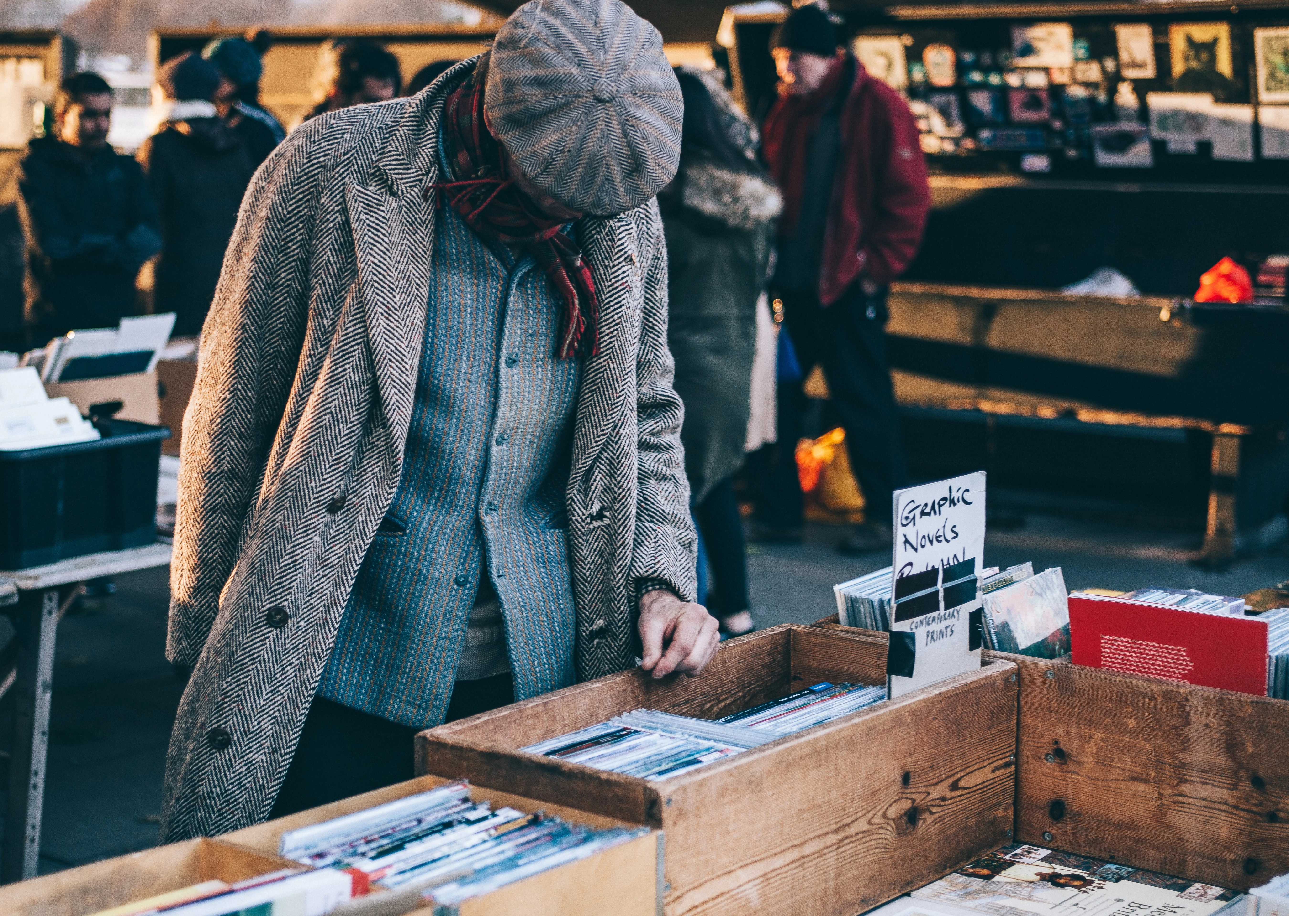 man at a flea market wearing a grey coat browsing books from wooden boxes